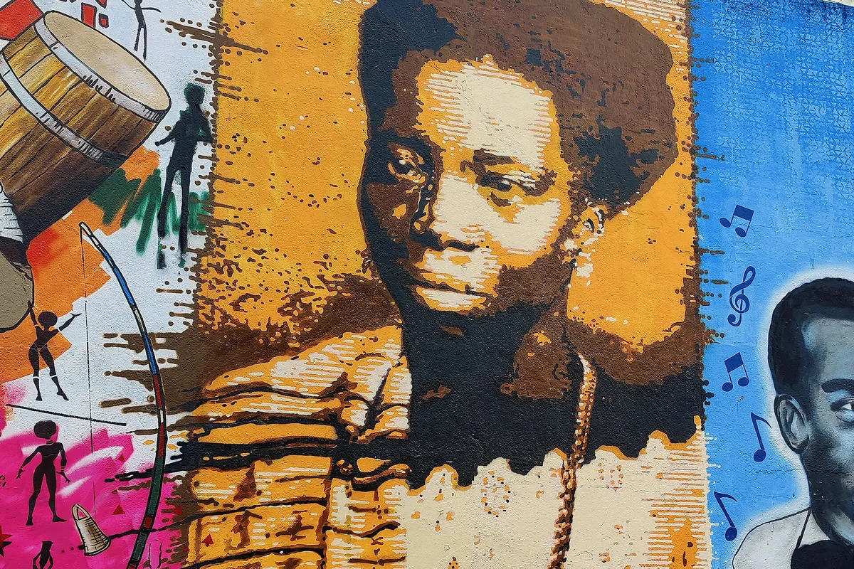 A large mural of Tia Ciata at Pedra do Sal in orange and brown tones, with drums and musical notes around her