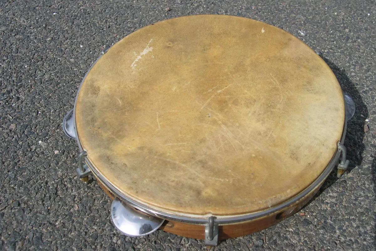 A pandeiro hand frame drum lying on the ground, showing its skin head and metal jingles in the wooden rim