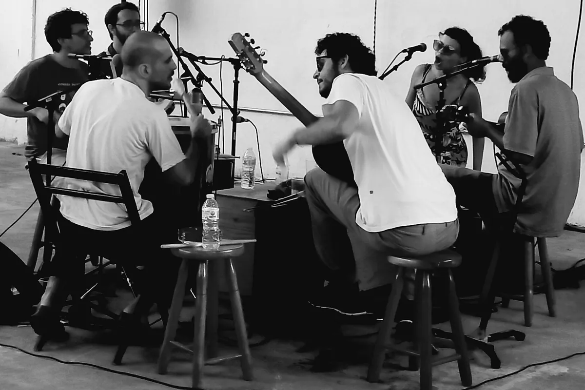 Black and white photograph of musicians with guitars and microphones seated on stools at a roda de samba