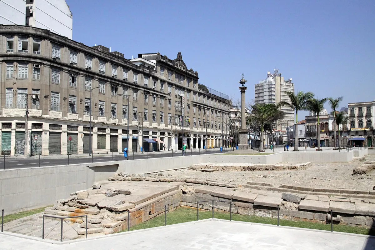 The excavated stone remains of the Valongo and Imperatriz wharves in a sunken plaza with a tall column behind
